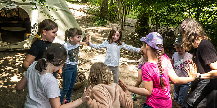 Pädagogin leitet eine Gruppe Kinder bei einem gemeinsamen Spiel im Wald – WaldErlebnisRaum, ein naturpädagogisches Angebot für Pädagog:innen und Interessierte