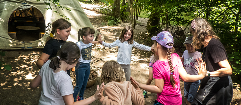 Pädagogin leitet eine Gruppe Kinder bei einem gemeinsamen Spiel im Wald – WaldErlebnisRaum, ein naturpädagogisches Angebot für Pädagog:innen und Interessierte